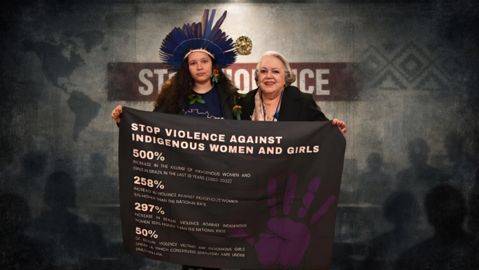 Jovem mulher indígena com cocar tradicional segura faixa denunciando a violência contra mulheres indígenas durante evento internacional.